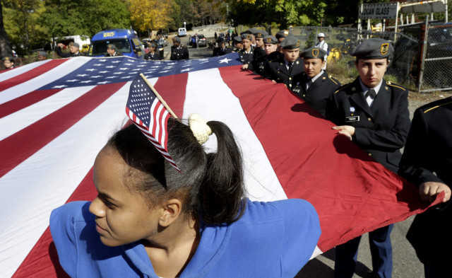 High school student Yomeidi Jose, 16, of Boston, wears a flag on her head while assisting other JROTC students in supporting an oversized American flag during a Columbus Day Parade in Boston, Oct. 12, 2014. (AP Photo)