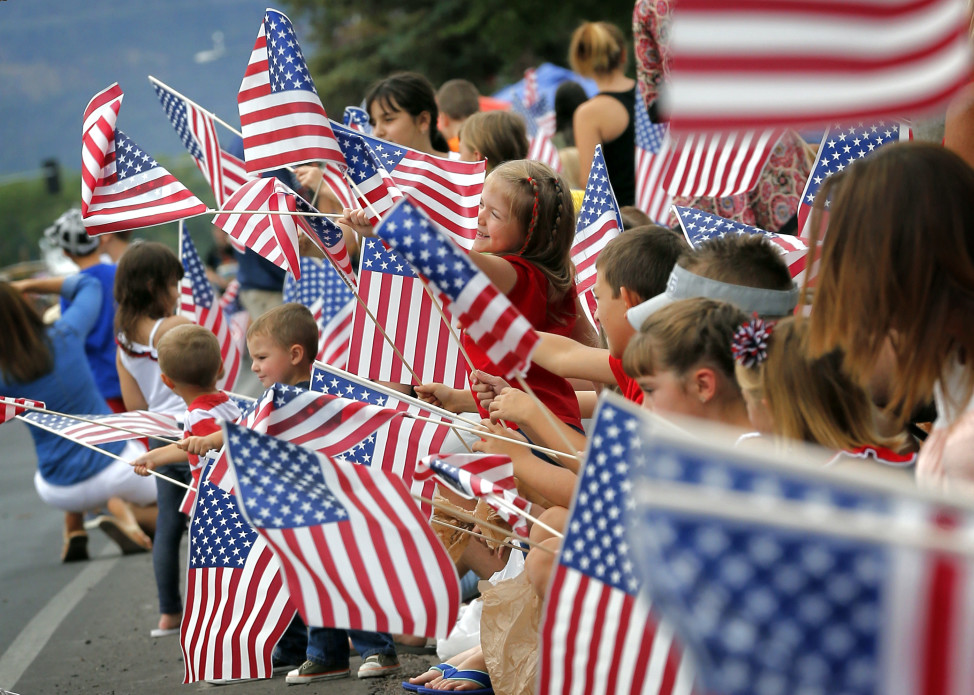 People wave flags as the Independence Day parade rolls down Main Street, July 4, 2014, in Eagar, Arizona. (AP Photo)