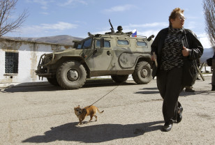 A woman walks her dog past an armed man, believed to be a Russian serviceman, standing guard outside a Ukrainian military base in Perevalnoye