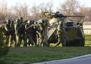 Armed men, believed to be Russian servicemen, take cover behind an armoured vehicle as they attempt to take over a military airbase in the Crimean town of Belbek near Sevastopol