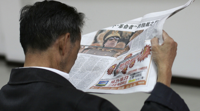 A man reads a local newspaper's story on the spread pages featuring a photo of Moammar Gadhafi