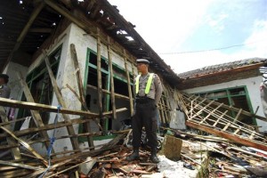 Seorang polisi berdiri di atas puing-puing rumah anggota Ahmadiyah yang diserang massa di Cikeusik, Senin (2/7).