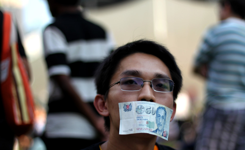 A man covers his mouth with a fifty dollar bill represent the lost of free speech at the Speakers Corner on Saturday, June 8, 2013 in Singapore to protest a new government policy requiring news websites to obtain licenses.