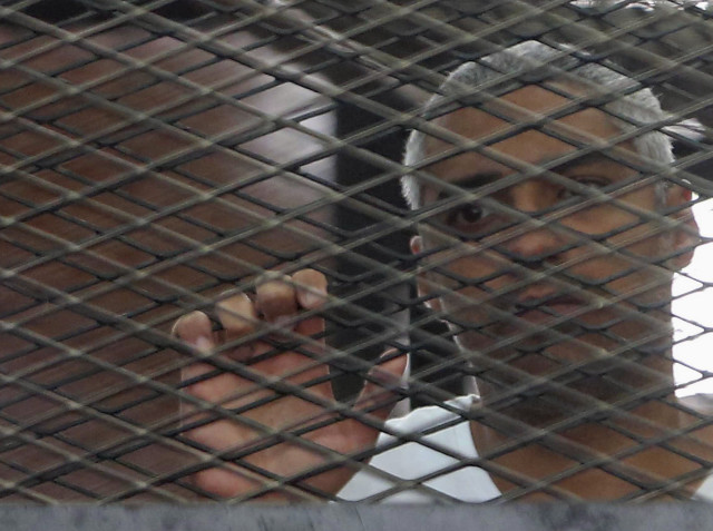Al Jazeera journalist Mohammed Fahmy stands behind bars at a court in Cairo May 15, 2014. REUTERS/Stringer
