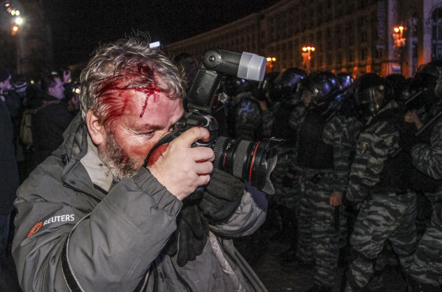 Wounded Reuters photographer Gleb Garanich, who was injured by riot police, takes pictures as riot police block protesters during a scuffle at a demonstration in support of EU integration at Independence Square in Kiev November 30, 2013. The International News Safety Institute says 58 journalists or media staff have been killed while working in 2014 alone. REUTERS