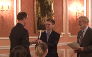 Ужин 9 октября. Томас (бывший сотрудник АНБ) вручает Эдварду Сноудену (экс-АНБ) свечу – символ премии Сэма Адамса, предполагающей освещение темных углов. (Кадр видео WikiLeaks)
