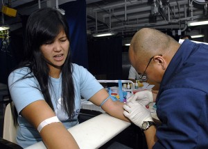 Young woman expresses her aversion to getting jabbed with a needle as a medical technician draws blood (Photo: US Navy)