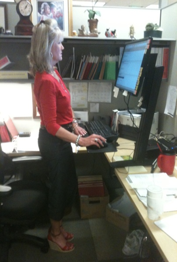 A woman using a sit-stand desk in its standing configuration. (National Institute for Occupational Safety and Health)