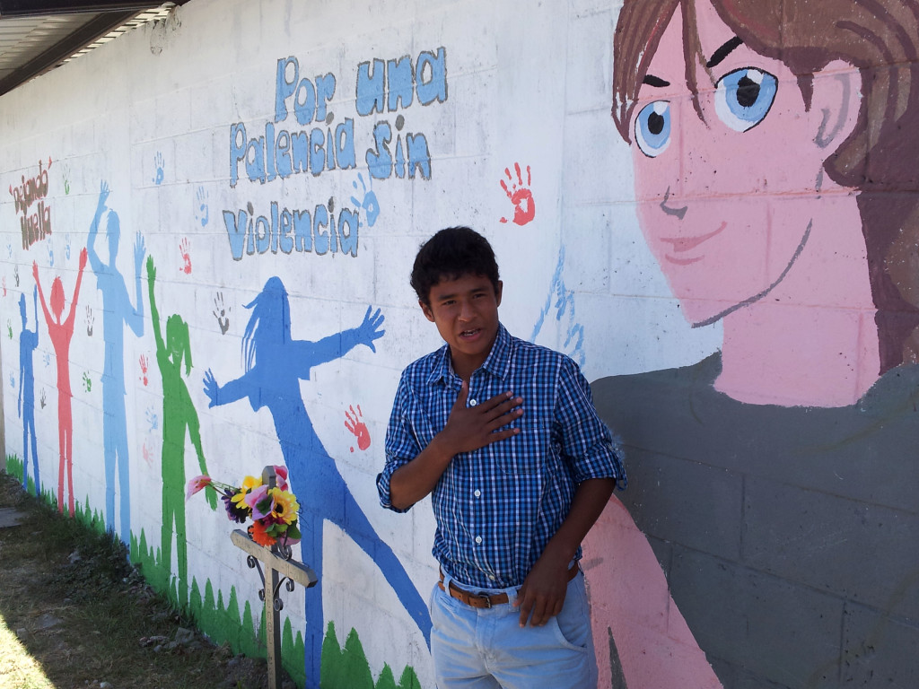 A youth in Palencia, Guatemala, who painted a mural on the wall in front of a stadium where one of his friends had been killed. The writing says “For a Palencia without Violence.” (ICMA)