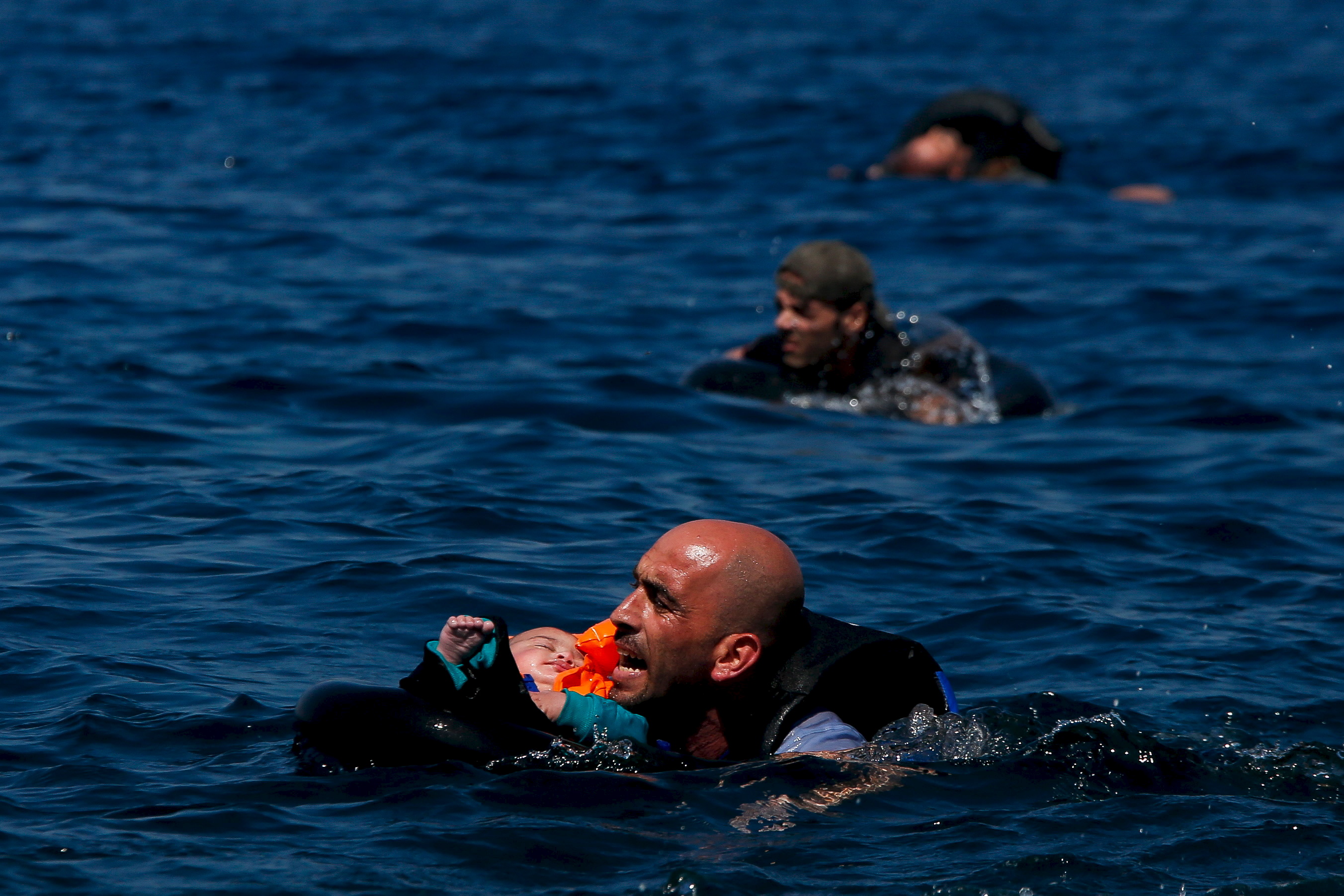 A Syrian refugee holding a baby swims towards the Greek island of Lesbos, Sept. 12, 2015, after another boat crammed with dozens of migrants and refugees deflated and sank. (Reuters)