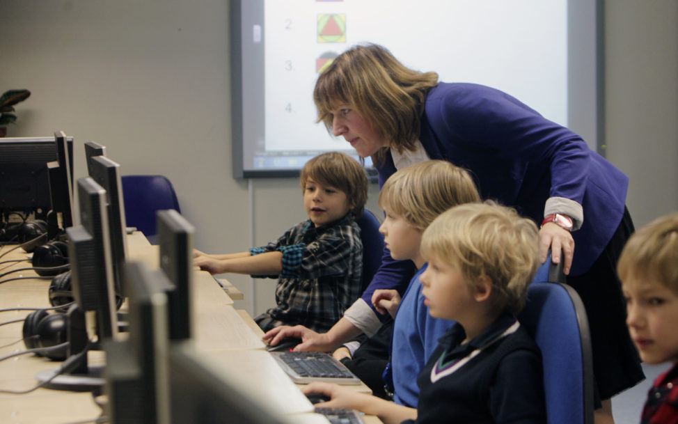 FILE - A teacher helps first grade students during a computer lesson in school in Tallinn, Estonia. (Reuters)