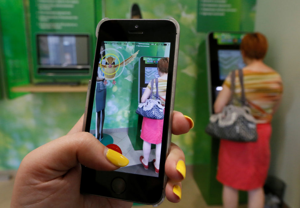 A woman plays the augmented reality mobile game 'Pokemon GO' by Nintendo, as a visitor uses an automated teller machine (ATM) in central Krasnoyarsk, Siberia, Russia, July 20, 2016. (Reuters)