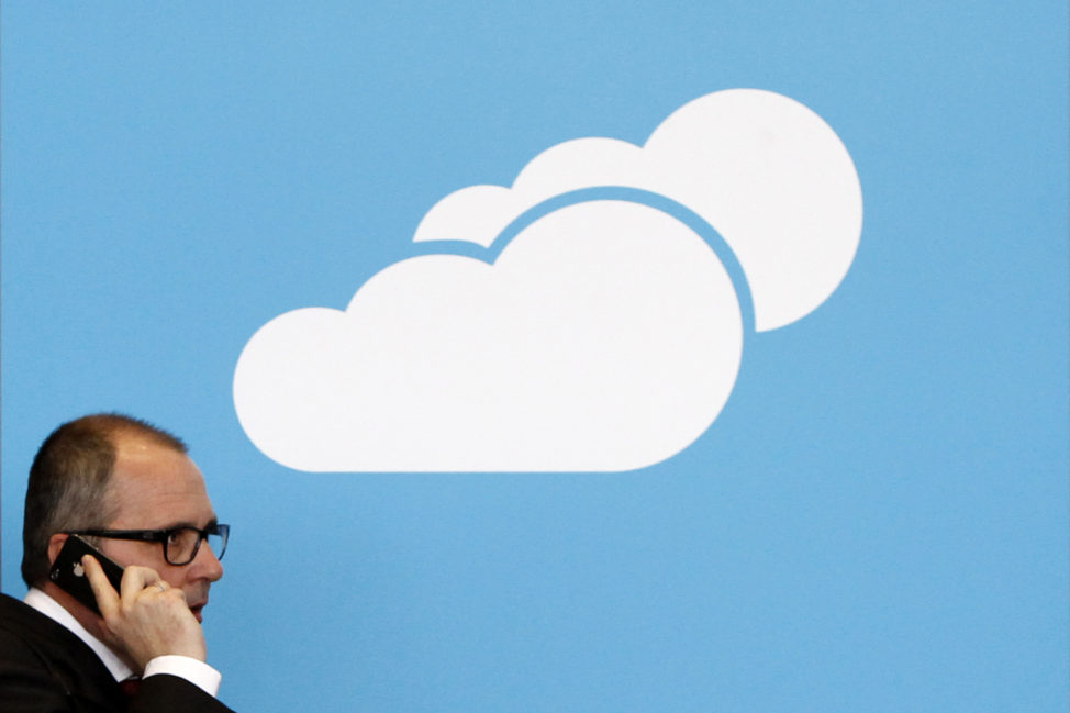 FILE - A visitor uses his mobile phone as he walks past the Microsoft booth with a logo for cloud computing software application in Hanover, Germany. (Reuters)