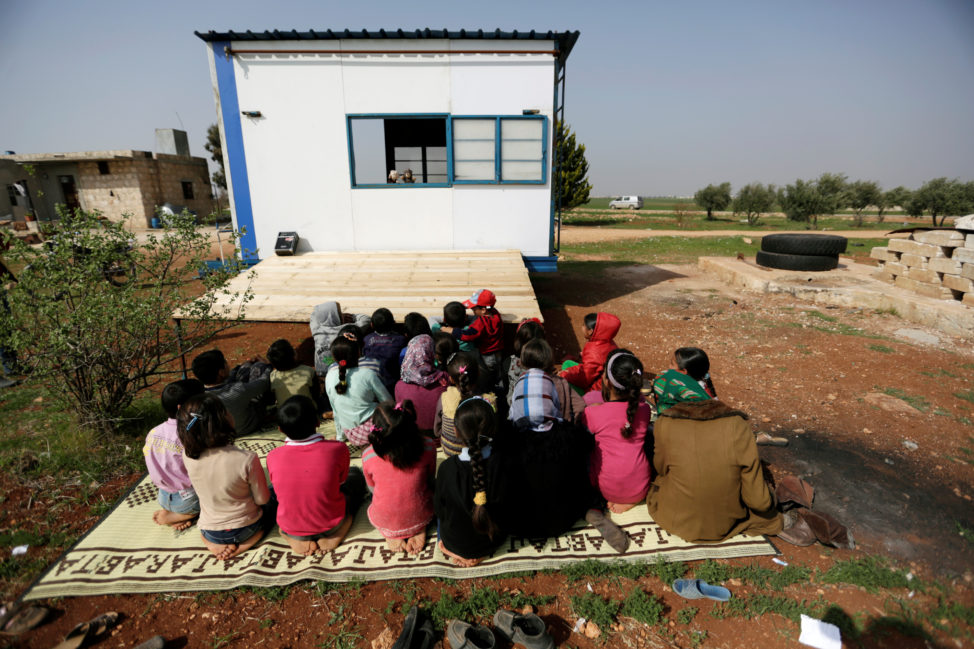 FILE - Children watch volunteer teachers perform a puppet show inside a mobile educational caravan for children who do not have access to schools on the outskirts of Saraqib, Idlib province, Syria, March 10, 2016.