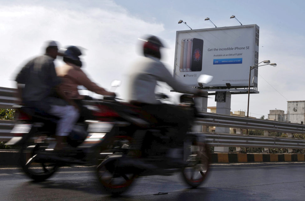 FILE - Men on motorbikes ride by an Apple iPhone SE advertisement billboard in Mumbai, India, April 26, 2016. (Reuters)