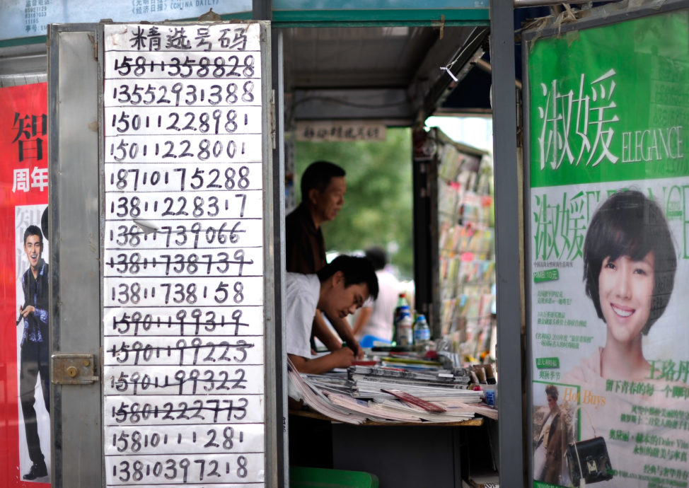 FILE - A vendor browses magazine at a news stand with a paper displaying mobile phone numbers for sale in Beijing. (AP)