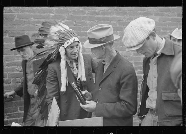 The fellow in the headdress is selling patent medicine at a medicine show in