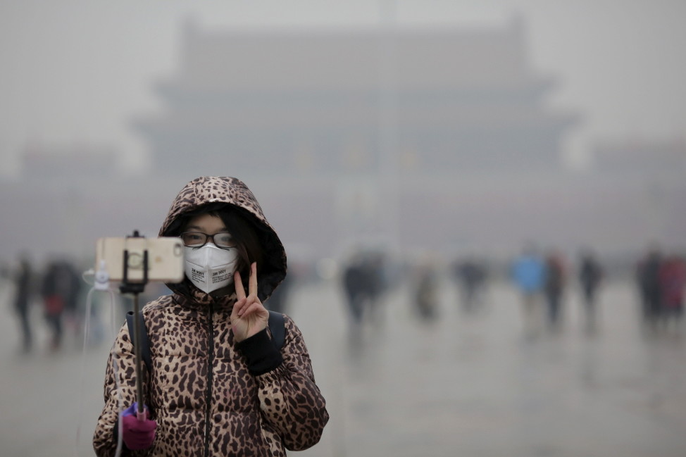 A woman wearing a protective mask has her picture taken just after a flag-raising ceremony amid heavy smog at the Tiananmen Square, after the city issued its first ever "red alert" for air pollution, in Beijing December 9, 2015. 