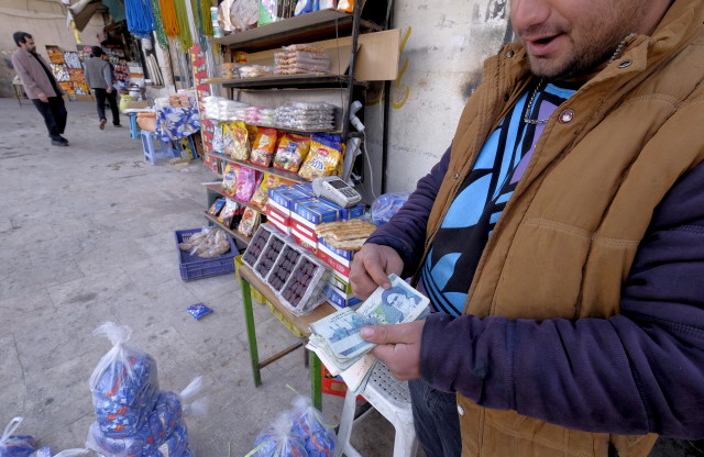 An Iranian shopkeeper counts money as he waits for customers in front of his shop in northern Tehran on Jan. 16, 2016. (Reuters)