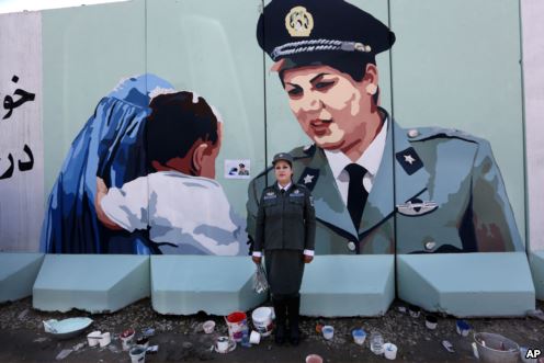 Friba Hameed, 30, an Afghan police officer, poses for a photograph in front of a mural of herself, painted by an independent artist, outside the main gate of a police precinct to mark International Women's Day in Kabul, Afghanistan, March 8, 2016.