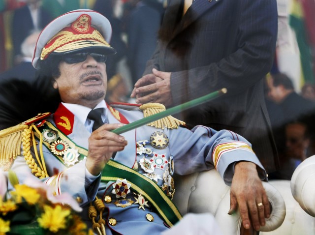 In this Sept. 1, 2009 file photo, Libyan leader Moammar Gadhafi gestures with a green cane as he takes his seat behind bulletproof glass for a military parade in Tripoli. (AP)