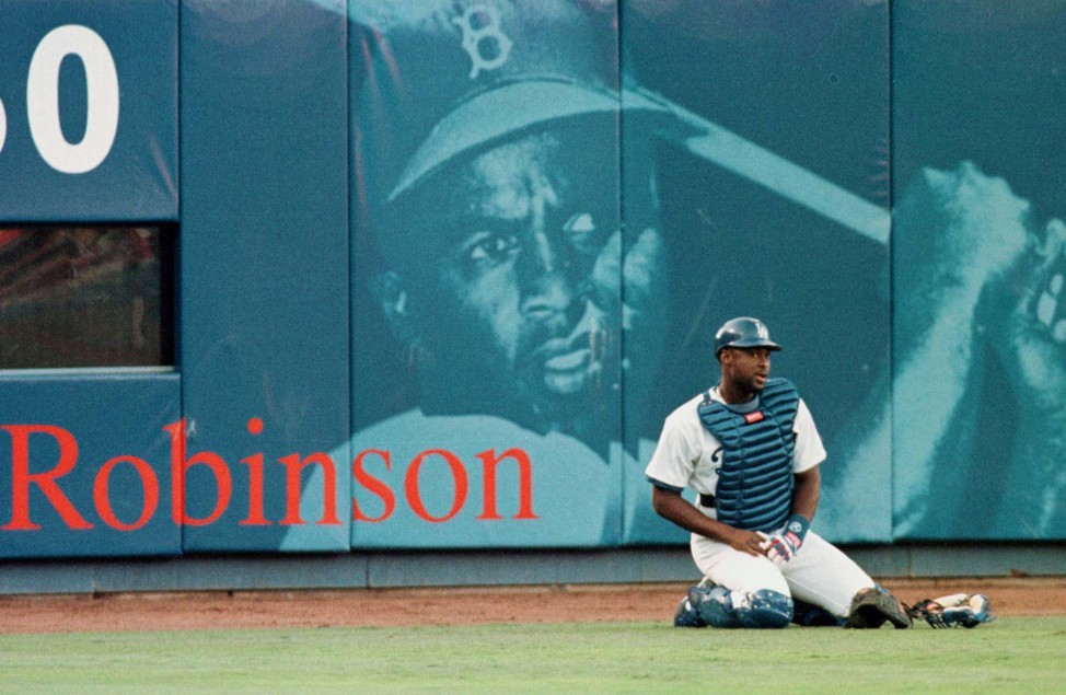 Los Angeles Dodgers catcher Charles Johnson stretches in front of a mural of baseball legend Jackie Robinson at Dodger Stadium before his debut game with the team May 16, 1998. (Reuters) 