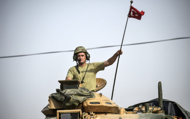 This picture taken around 5 kilometres west from the Turkish Syrian border city of Karkamis in the southern region of Gaziantep, on August 25, 2016 shows a soldier gesturing as Turkish Army tanks drive to the Syrian Turkish border town of Jarabulus. (AFP)  