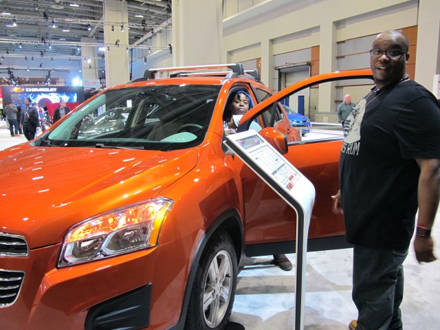 A vibrant orange Chevrolet Trax SUV attracts Phillip Akinola and his fiancee, Kyra Taylor, sitting in the driver's seat with their baby daughter at the Washington Auto Show, Jan. 28, 2016. The family, from Largo, Md., generally steers toward more conservative car colors. (C. Guensburg/VOA)