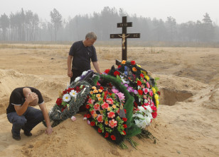 The husband and a son of Natalia Ivleva, 47, a wildfire victim who fell sick while helping to extinguish a fire in the settlement of Mokhovoye, mourn at her grave in Beloomut