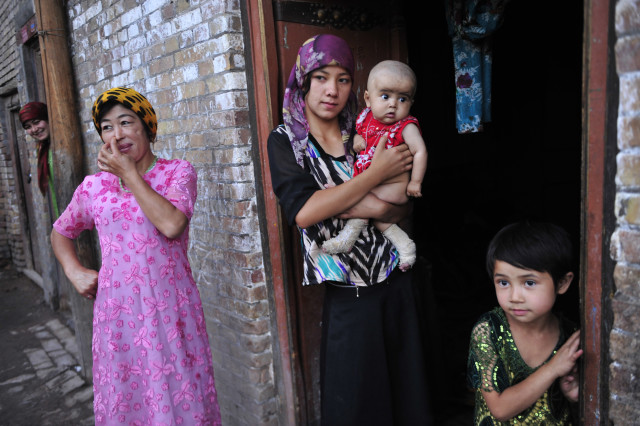 An ethnic Uighur woman (C) hugs her son as she stands outside her house with her daughter (R) and neighbours at an old residential area of Kashgar, Xinjiang Uighur Autonomous Region July 22, 2012.  REUTERS/Rooney Chen 