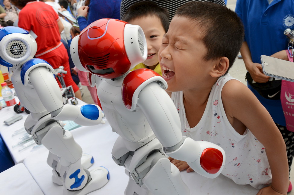 A boy tries to talk with a humanoid robot during a science event in the Chinese province of Henan province on 9/19/15. (Reuters)