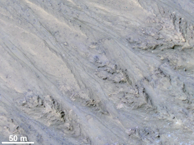 This HiRISE image cutout shows Recurring Slope Lineae in Tivat crater on Mars in enhanced color. The narrow, dark flows descend downhill (towards the upper left). Analysis shows that the flows all end at approximately the same slope, which is similar to the angle of repose for sand.​​​​​​​ (NASA/JPL/University of Arizona/USGS/Public Domain)