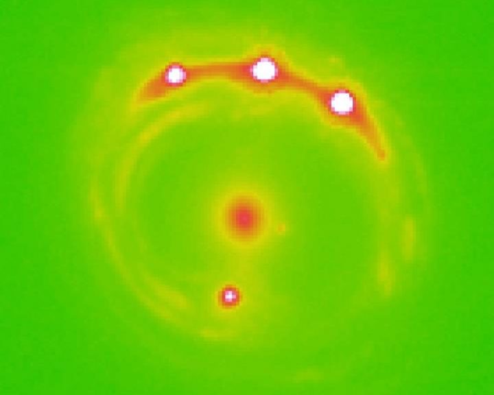 Image of the gravitational lens RX J1131-1231 galaxy with the lens galaxy at the center and four lensed background quasars. University of Oklahoma research estimate that there are trillions of planets in the center elliptical galaxy in this image. (University of Oklahoma)