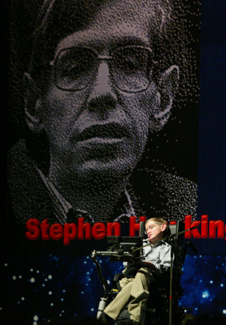 Renowned physicist Stephen Hawking is wheeled into an auditorium in Beijing before giving a speech on Aug. 18, 2002. Hawking, known for his theories about black holes and other properties of the universe, gave a speech to a mostly student audience about how space-time exists in up to 11 dimensions. (AP Photo/Greg Baker)