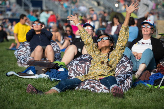 People are seen as they watch a total solar eclipse through protective glasses in Madras, Oregon on Monday, Aug. 21, 2017 - the Great American Eclipse. (NASA/Aubrey Gemignani, Public Domain via Flickr)