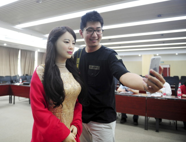 A man takes pictures with humanoid robot Jiajia produced by University of Science and Technology of China, at Jiajia's launch event in Hefei, Anhui province, April 15, 2016. Jiajia can converse with humans and imitate facial expressions, among other features. b (Reuters/China Stringer Network)