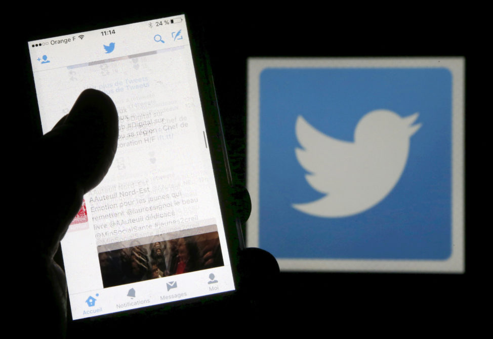 FILE - A man reads tweets on his phone in front of a displayed Twitter logo in Bordeaux, southwestern France, March 10, 2016. (Reuters)