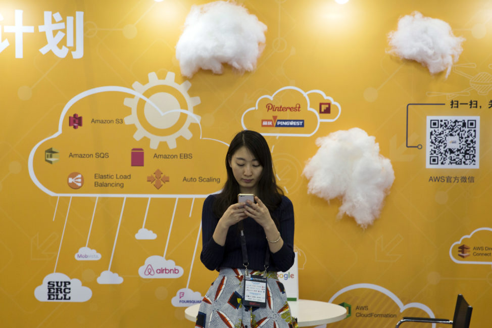 FILE - A woman uses her smartphone near a booth promoting cloud services during the Global Mobile Internet Conference in Beijing, China, April 29, 2016. (AP)