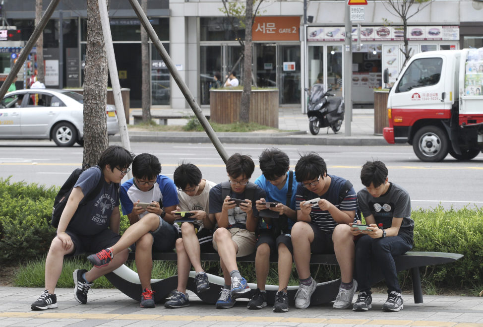 FILE - South Korean high school students play games on their smartphones on a bench on the sidewalk in Seoul, South Korea. (AP)