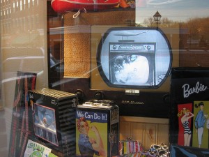 Here’s a display of old-timey things, including an early television set.  Not so early, however, that it didn’t have commercials.  This one, ironically, is advertising another vintage TV and console.  (Old Onliner, Flickr Creative Commons)