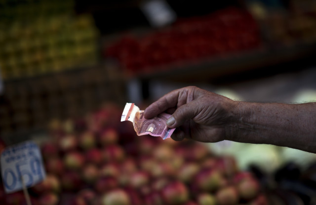 A man holds out a ten euro bill to pay for produce in a fruit market in Athens on July 7, 2015. 