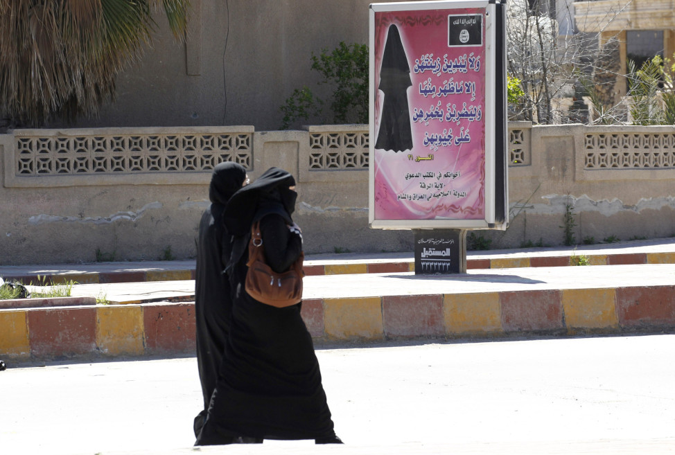 Veiled women walk past a billboard inscribed with a verse from Koran, urging women to wear a hijab in the northern province of Raqqa on Mar. 31, 2014.