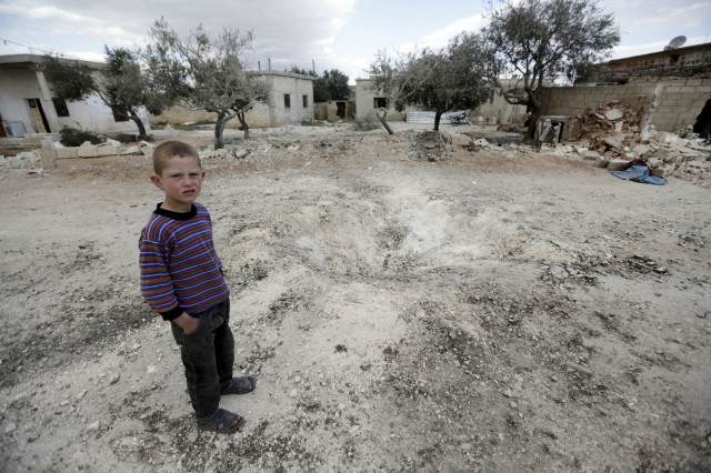 A boy stands near a hole in the ground after a shell fell in the rebel-held town of Jarjanaz, southern Idlib countryside, Syria March 5, 2016. (Reuters)