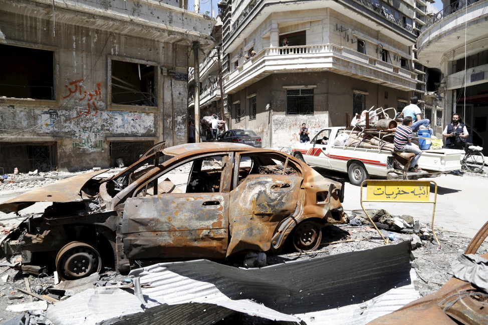 A truck drives past a vehicle, damaged during the Syrian conflict between government forces and rebels, Homs, Syria May 13, 2014. (Reuters)