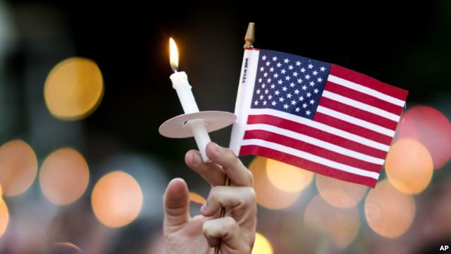 A mourner holds up an American flag and a candle during a vigil for a fatal shooting at an Orlando nightclub, June 12, 2016, in Atlanta.