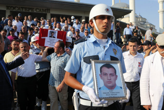 A Turkish Police officer holds a picture of one of the police officers killed during the failed July 15 coup attempt as other police officers carry the coffin during a funeral ceremony in Ankara on July 18, 2016.  Turkey launched fresh raids and sacked almost 9,000 officials today in a relentless crackdown against suspects behind an attempted coup that left over 300 people dead, as Western allies warned against reinstating the death penalty. / AFP PHOTO / ADEM ALTAN