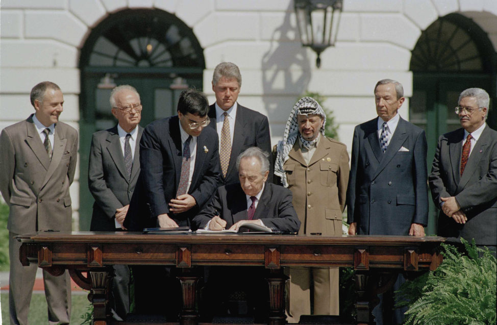 Israeli Foreign Minister Shimon Peres signs the Mideast Peace Agreement on the South Lawn of the White House in Washington, D.C., as President Clinton, standing center, PLO Chairman Yasser Arafat, third from right, and other dignitaries look on, Sept. 13, 1993. From left to right are: Russian Foreign Minister Andrei Kozyrev; Israeli Prime Minister Yitzhak Rabin; an unidentified aide; Clinton; Peres; Arafat; Secretary of State Warren Christopher; and Arafat aide Mahmoud Abbas. (AP) 